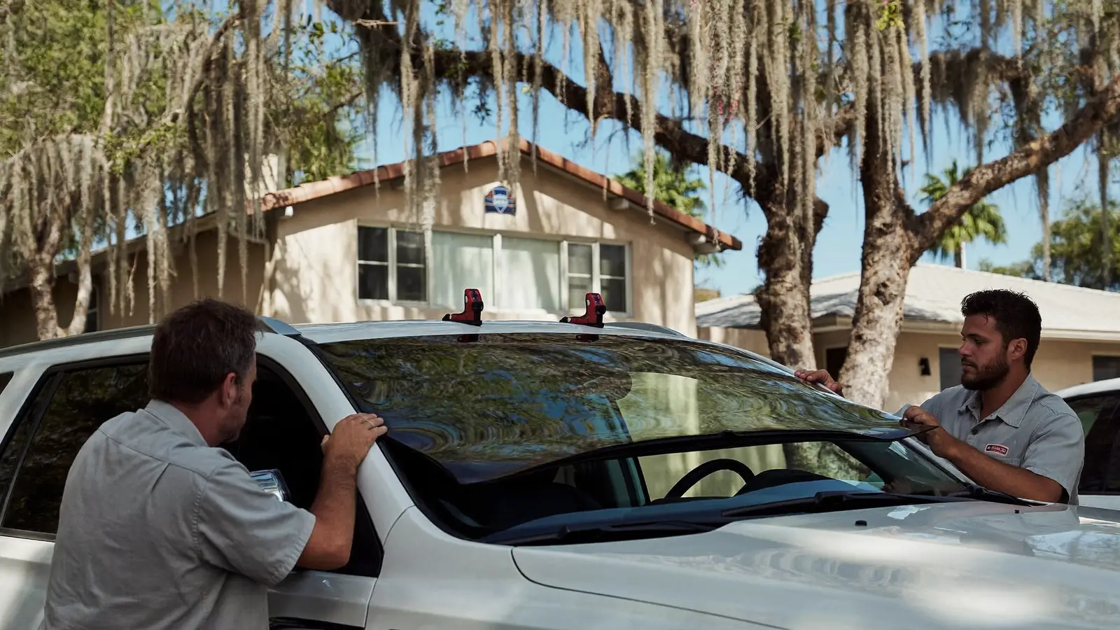 Two auto glass technicians setting a new windshield on an SUV in a driveway