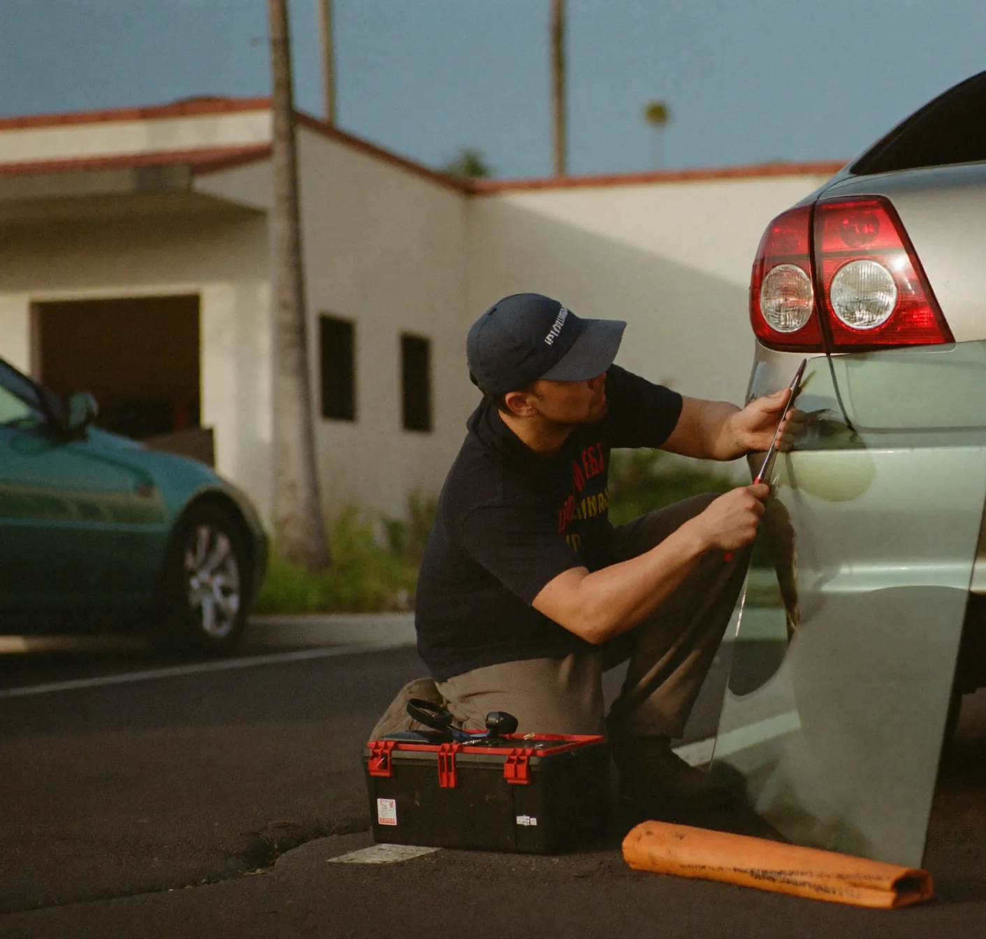 Auto glass technician kneeling beside a car with new glass on a stand